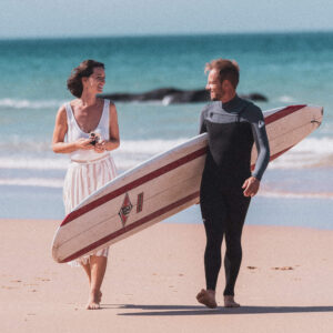 Homem com uma prancha de surf caminhando com uma mulher pela praia