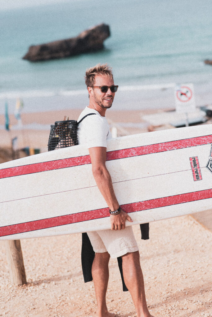 Homem a sorrir com uma prancha de surf numa praia